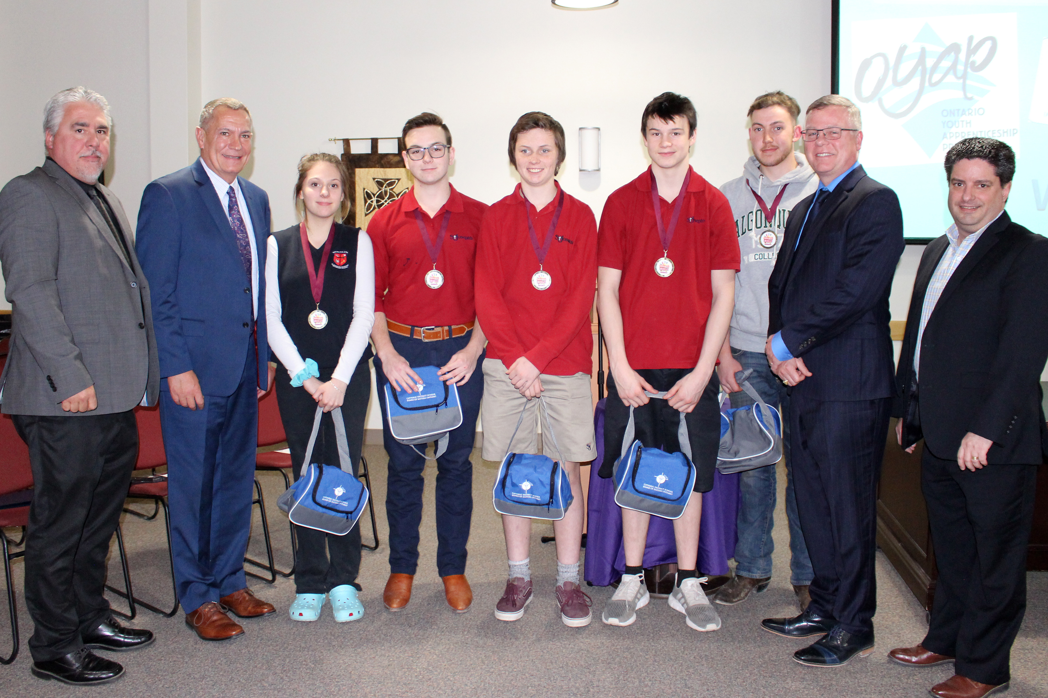 Students who attended the Eastern Ontario Skills Competition present information to the Board of Trustees. Students stand with board administrators and teacher.